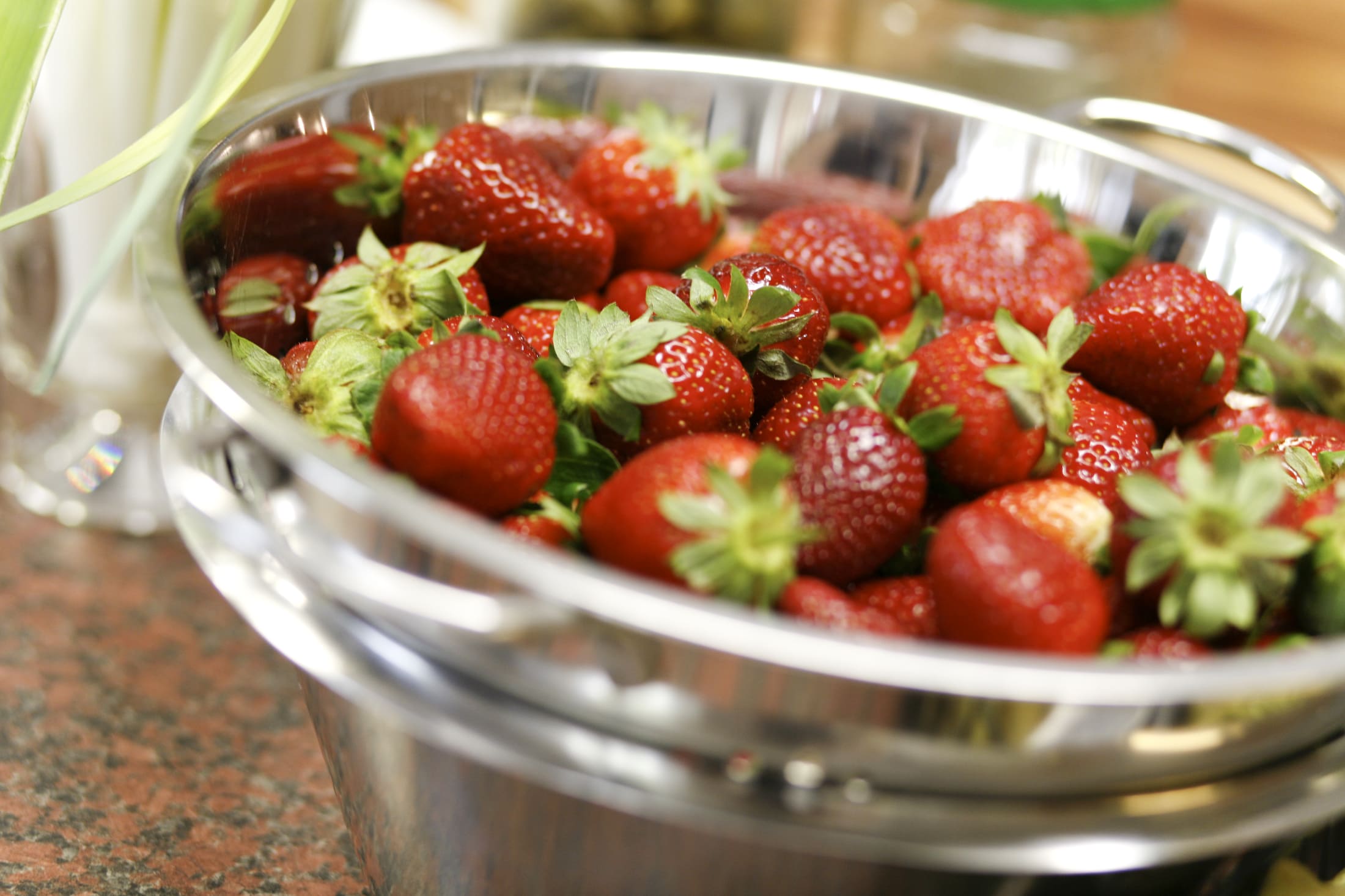 Reife Erdbeeren glänzen in einer Metallschale.